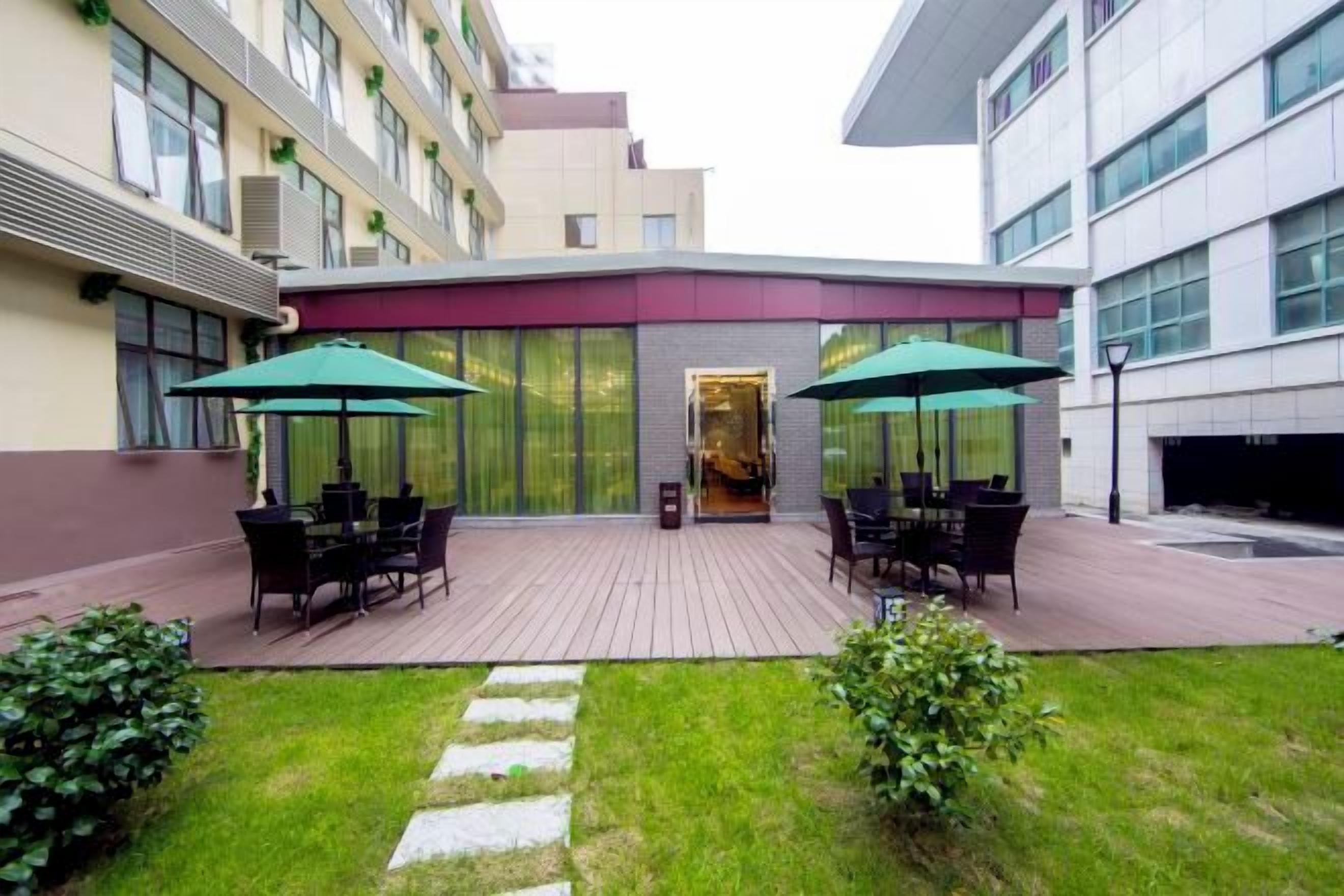 Un patio al aire libre con mesas y sillas, un césped y la entrada de un edificio.