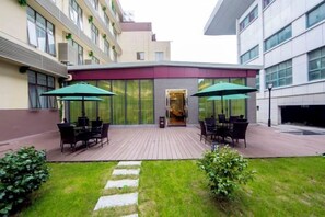 Un patio al aire libre con mesas y sillas, un césped y la entrada de un edificio.