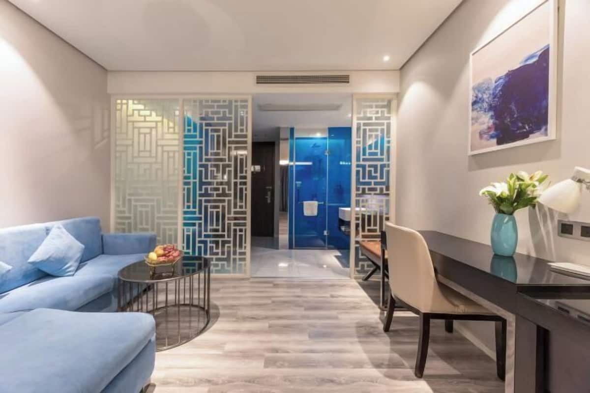 Una habitación de hotel moderna con sofá, mesa de comedor, un jarrón con flores y una pared azul decorativa.