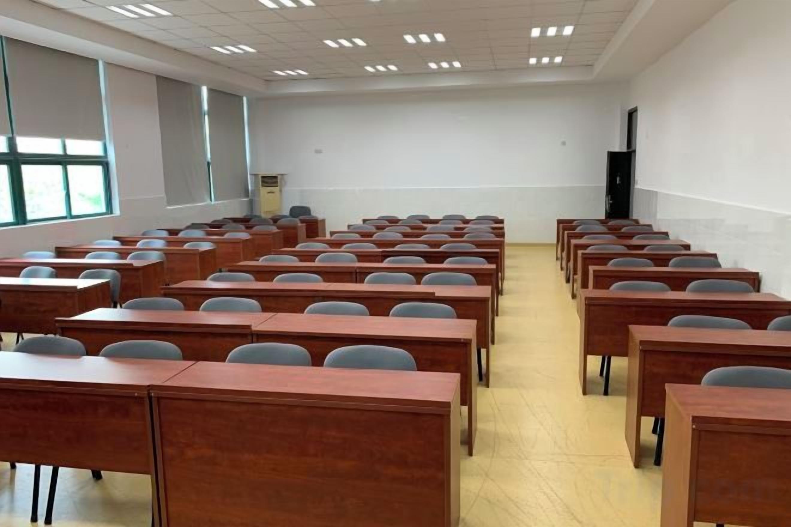 A classroom with rows of desks and chairs, a projector screen, and a large window.