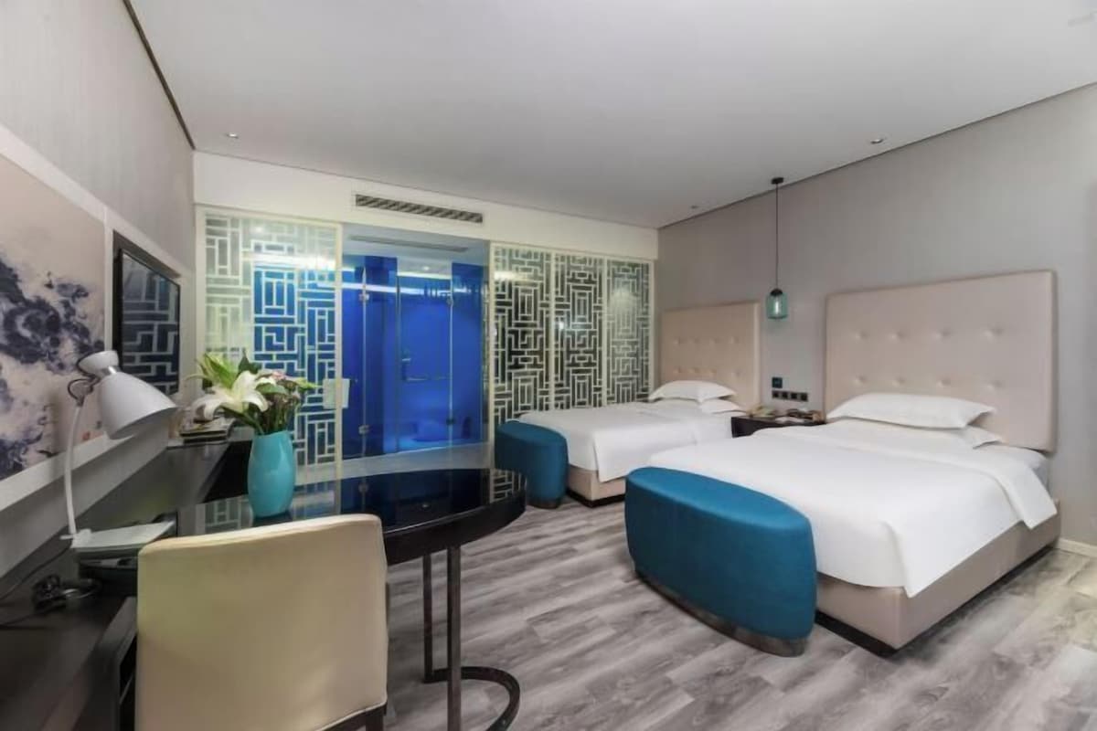 Ein Hotelzimmer mit Schreibtisch, zwei Betten, einer blauen Akzentwand und einem dekorativen Raumteiler.
