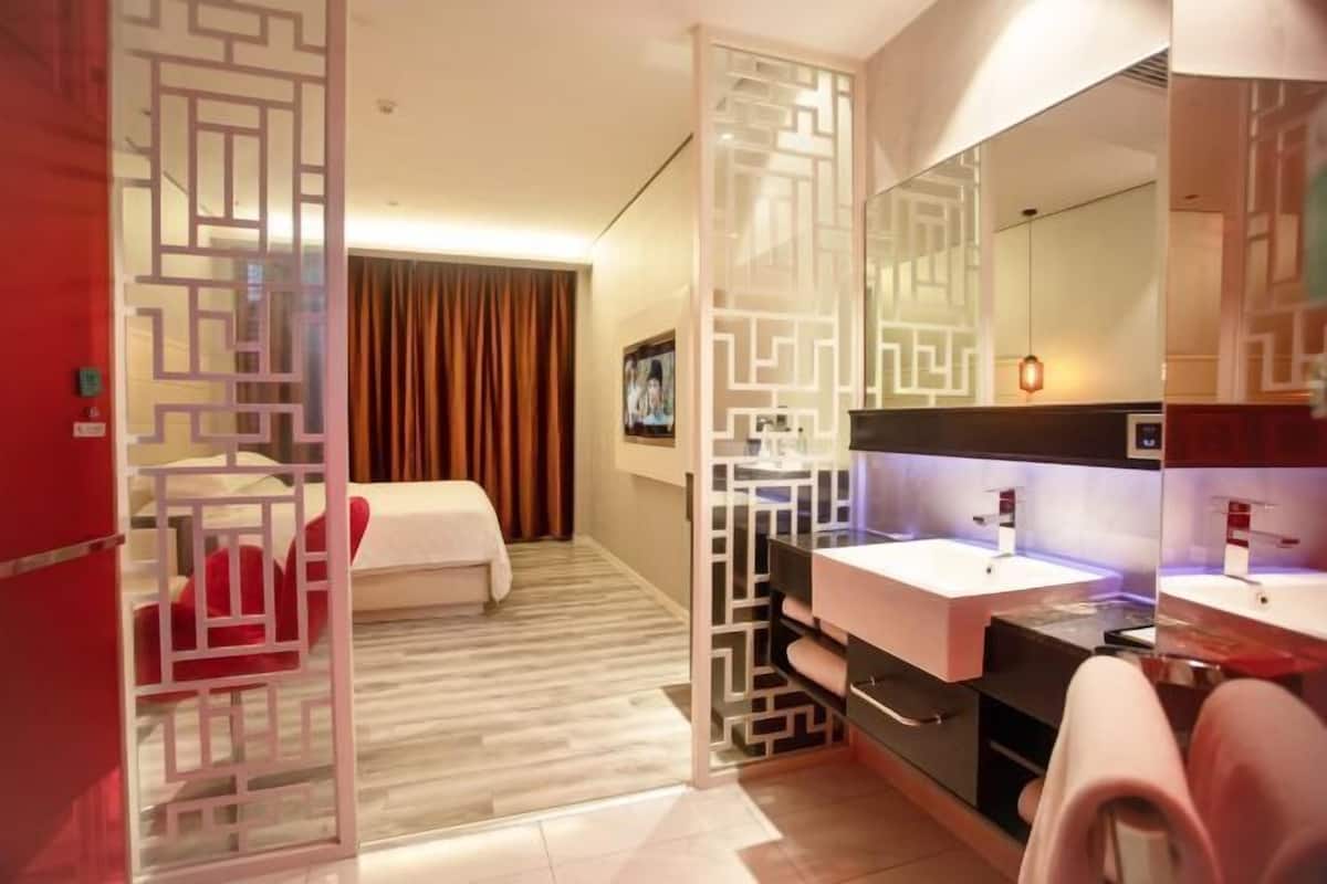 Una habitación de hotel con una cama, un espejo grande, un lavabo blanco y un separador decorativo.