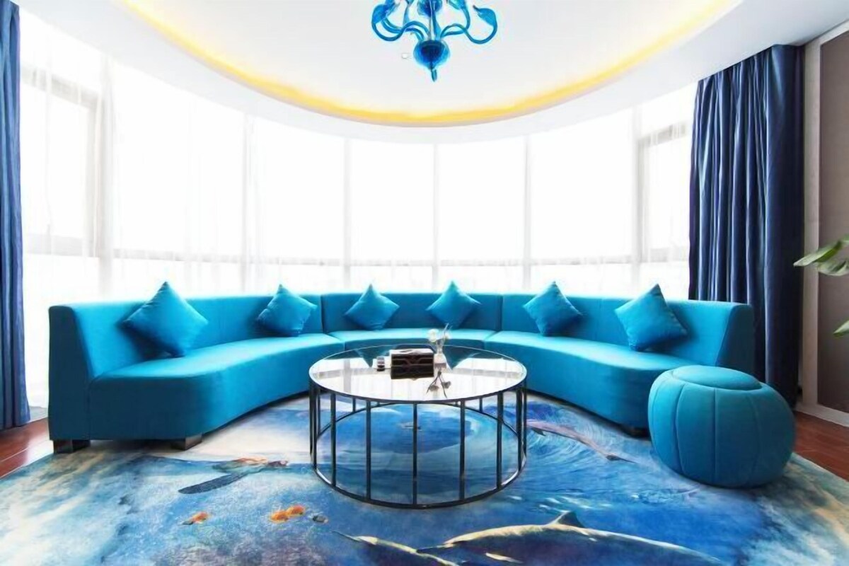 Ein modernes Wohnzimmer mit einem blauen Sofa, einem Glastisch und einem großen Fenster mit Vorhängen.