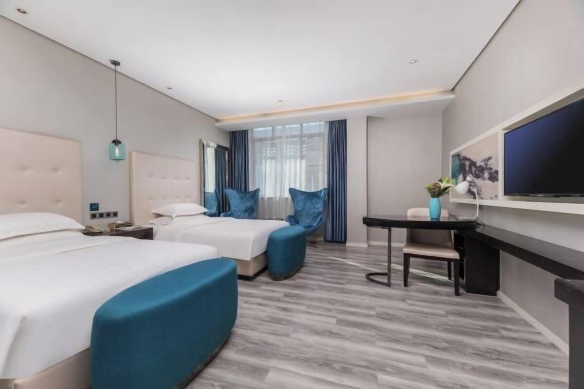 Habitación de hotel con dos camas, un escritorio, una silla, un televisor y una ventana con cortinas.
