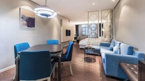 Una habitación de hotel moderna con zona de comedor, sofá, cama y un panel decorativo en la pared.