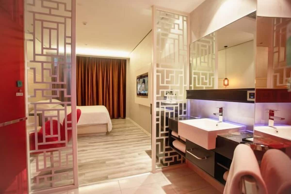 Habitación de hotel con cama, baño con espejo, lavabo y una partición decorativa.