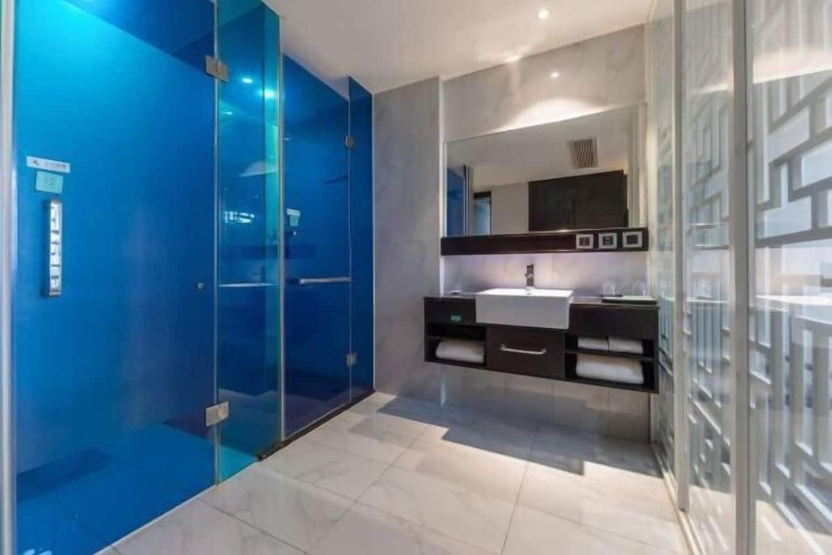Un baño moderno con cabina de ducha de vidrio, un lavabo blanco y un mueble de tocador oscuro.