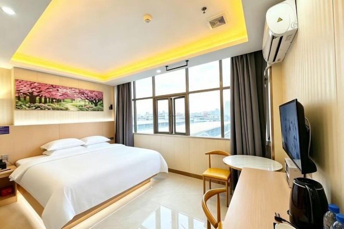 A hotel room with a bed, a desk, a chair, a TV, and a window with a city view.