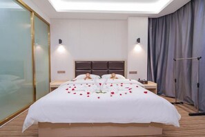 A hotel room with a large bed, bedside tables, a headboard, and a curtain on one side.