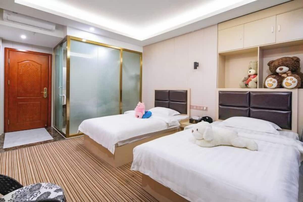 A hotel room with two beds, a wardrobe, a bedside table, and a shelf with teddy bears.