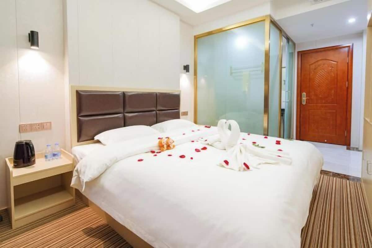 A hotel room with a large bed, a bedside table with a coffee maker, and a wardrobe with a glass door.