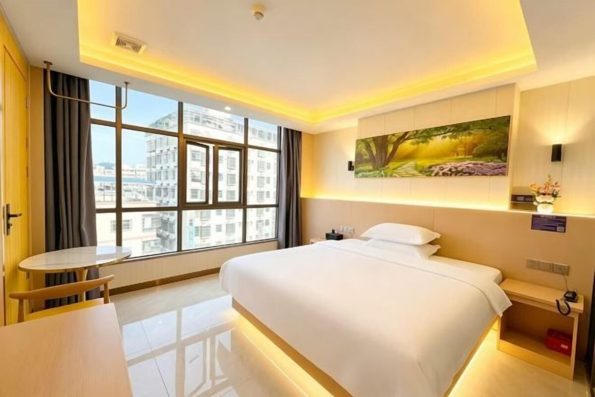 A hotel room with a large bed, a desk, and a window with a city view.