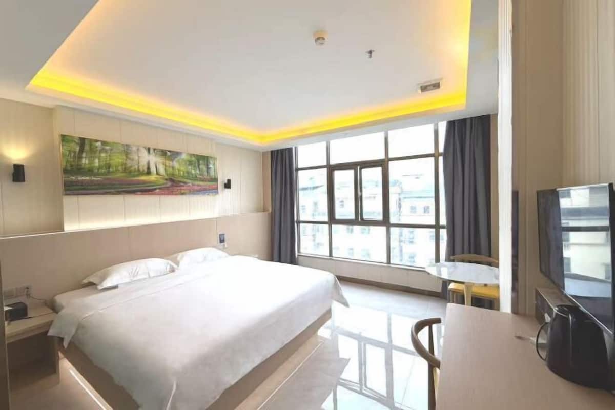 A hotel room with a large bed, a desk, a chair, a television, and a window with curtains.