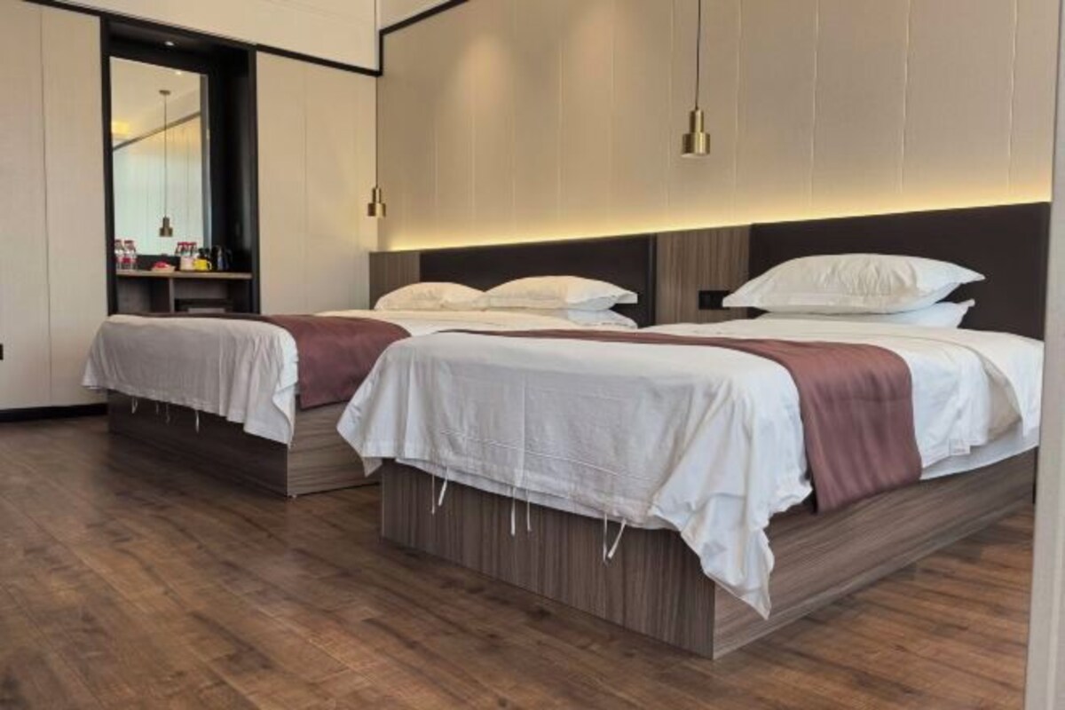 A modern hotel room with two beds, wooden flooring, and a large mirror.