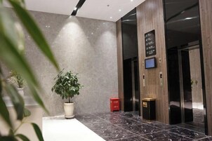 Un vestíbulo con una planta en maceta, un panel informativo digital y un cubo de basura.