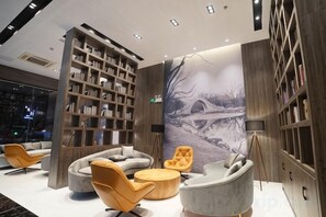 A modern interior with a large bookshelf, seating area, and a mural. - GYA Hotel (Yancheng Wengang Road High-speed Railway Station) (Yancheng)
