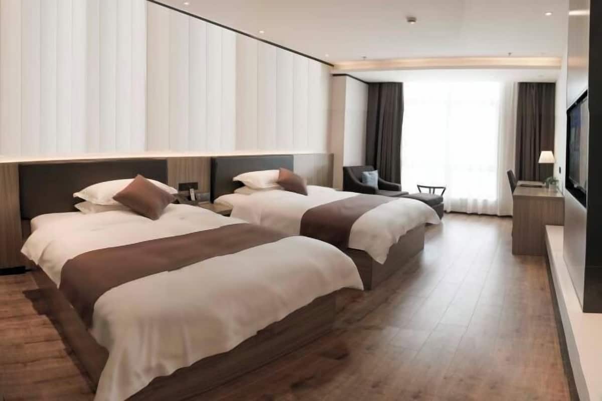 A hotel room with two beds, a desk, and a TV.