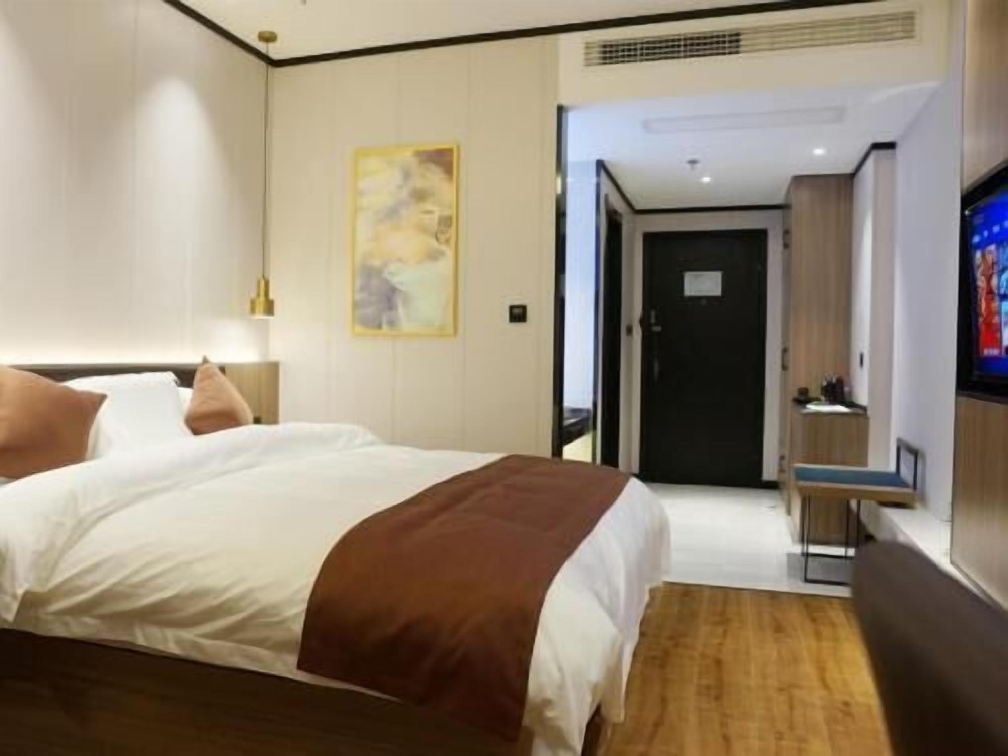 A hotel room with a bed, a desk, a television, and a door leading to another room.