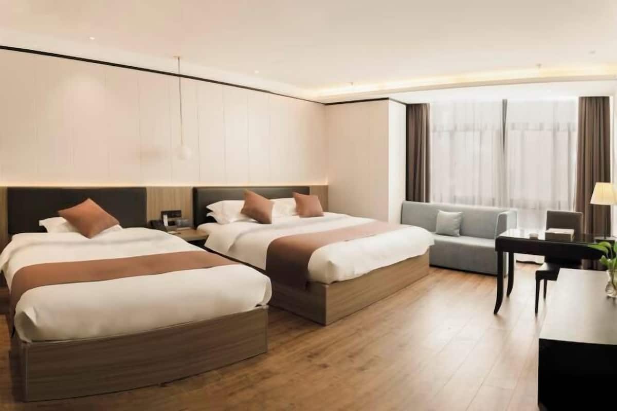 A hotel room with two beds, a sofa, a desk, and a large window with curtains.