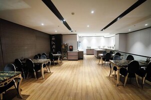 Un comedor con varias mesas y sillas, una cocina al fondo y suelo de madera.