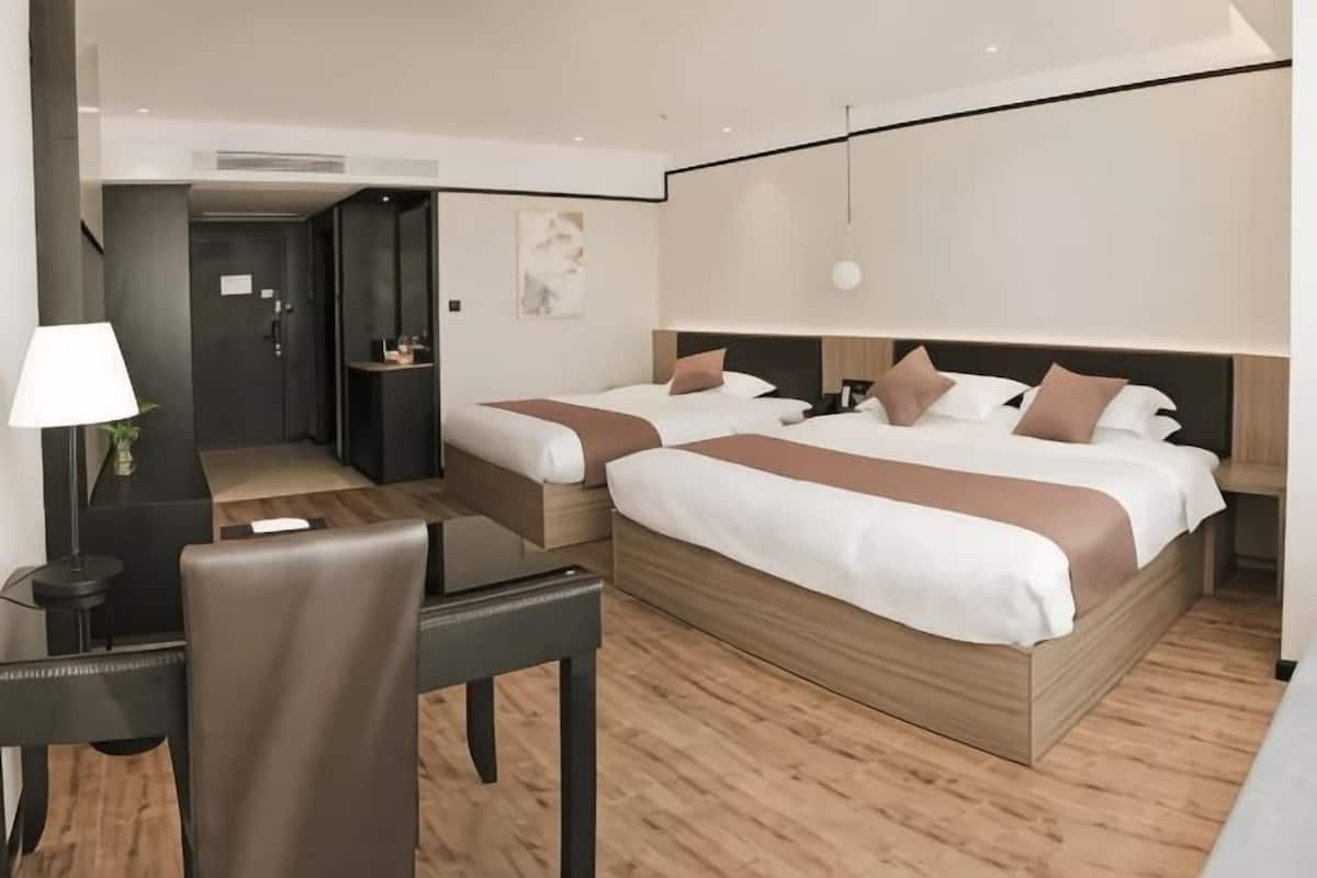 A hotel room with two beds, a desk, a chair, a lamp, and a small table.