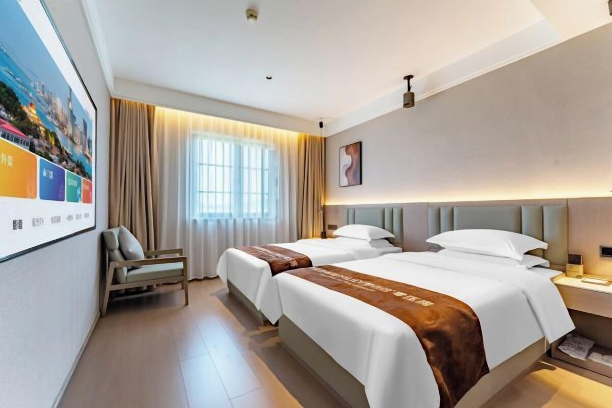 A hotel room with two beds, a desk, a chair, and a large window with curtains.