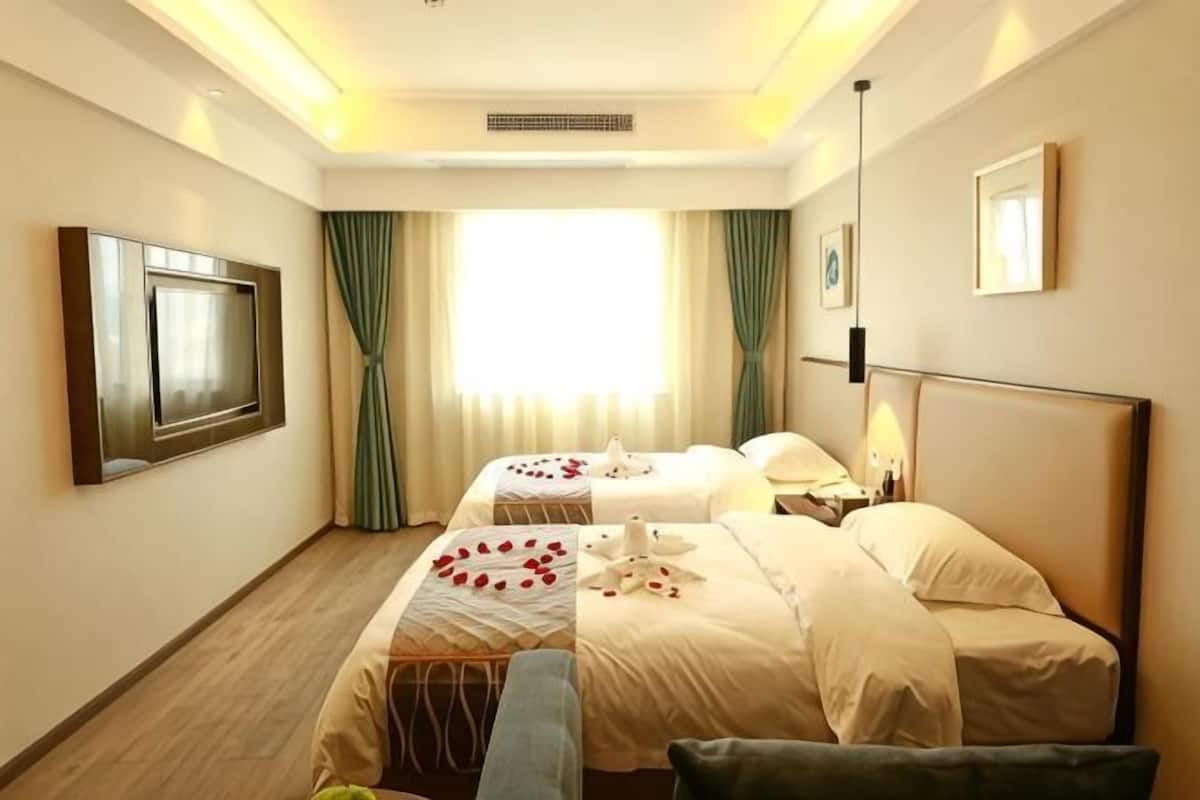 A hotel room with two beds, a TV, a desk, and a window with curtains.