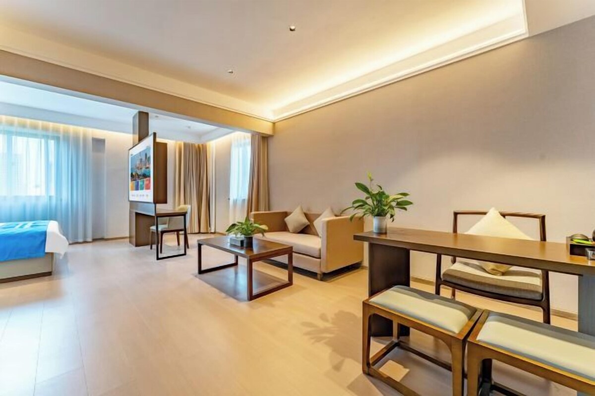 A modern hotel room with a sofa, a dining table, a coffee table, and a TV.