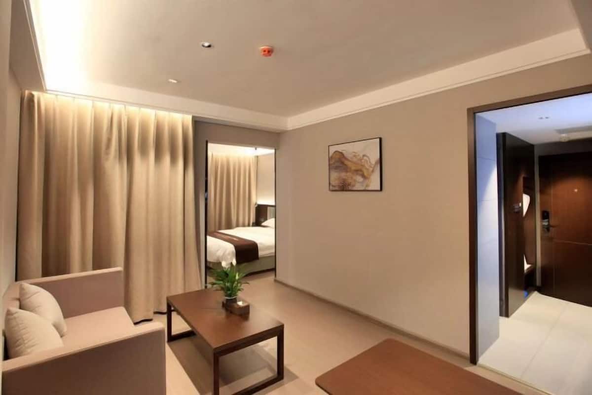 A modern hotel room with a sofa, a small table with a plant, a bed, and a painting on the wall.