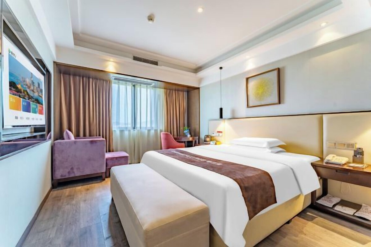 A hotel room with a large bed, a desk, a chair, a sofa, and a television.