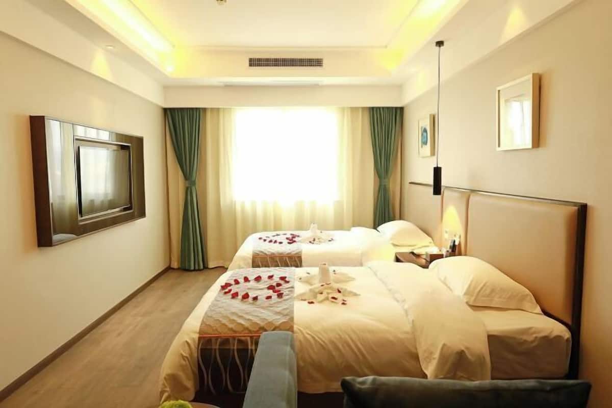 A hotel room with two beds, a TV, a bedside table, and a window with curtains.