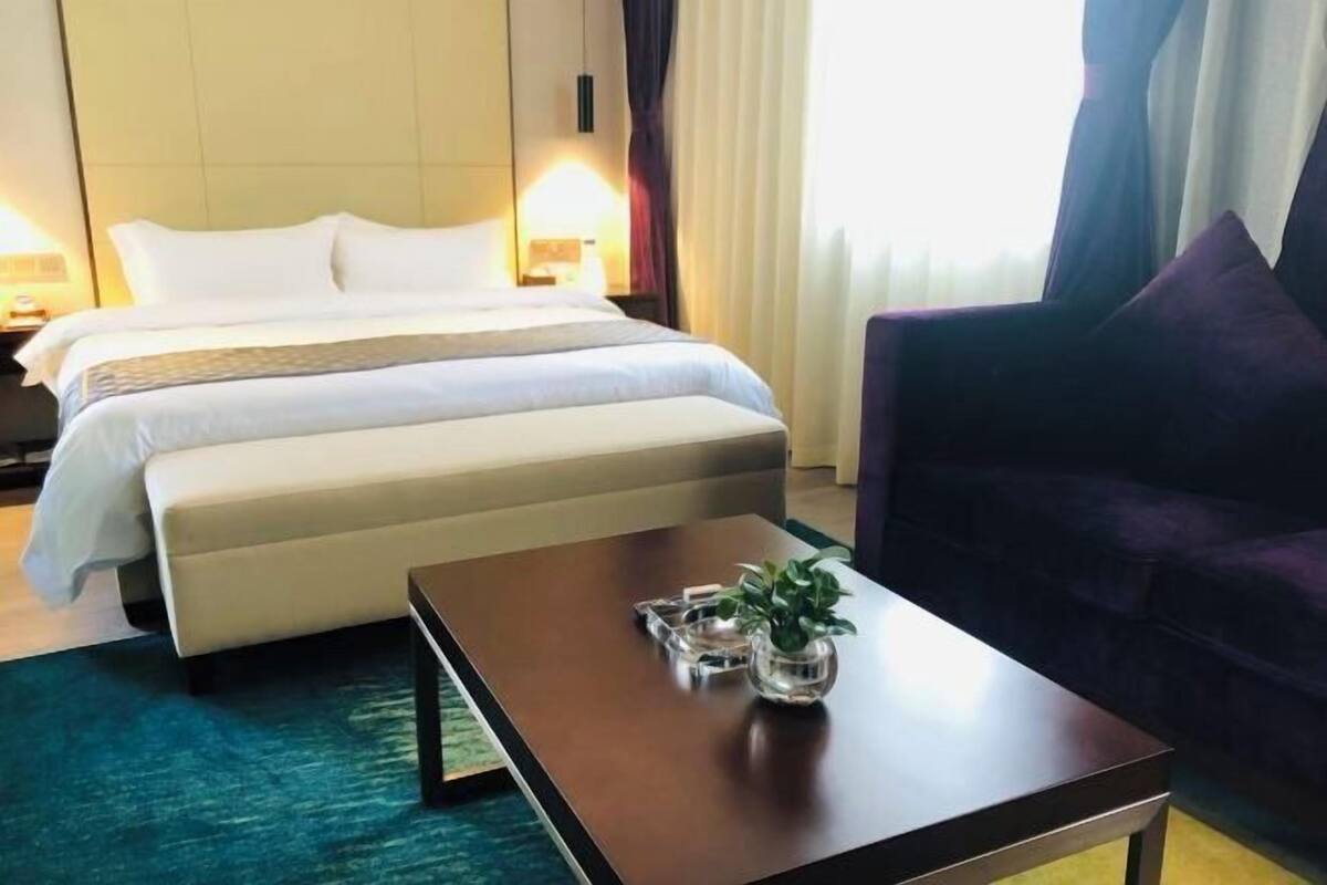 A hotel room with a bed, a sofa, a coffee table with a plant, and a nightstand with a lamp.