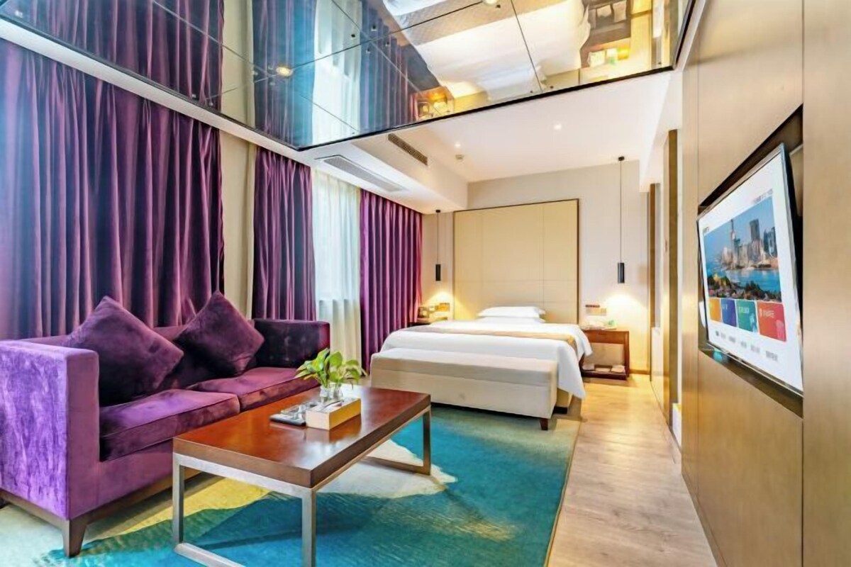 A hotel room with a bed, a sofa, a coffee table, and a large window.