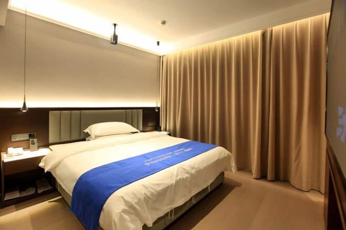 A hotel room with a large bed, a bedside table with a lamp, and a curtain on the window.