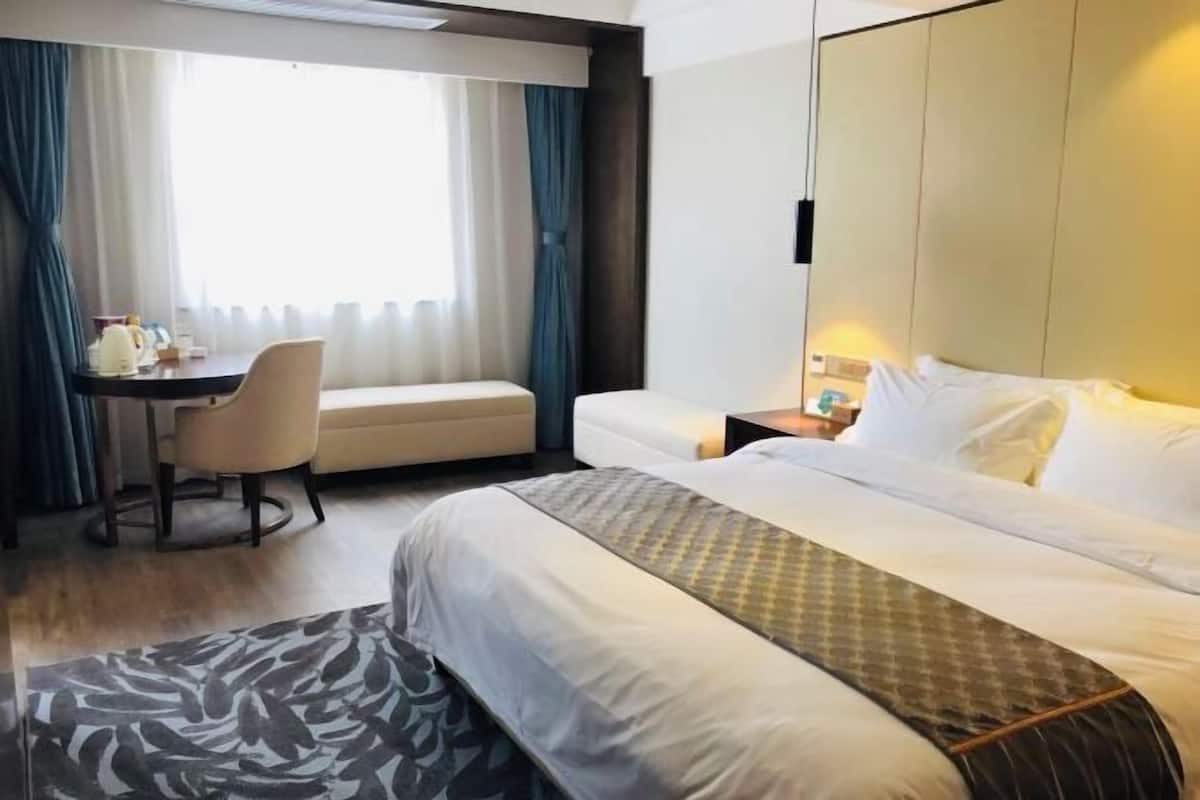 A hotel room with a bed, a desk, a chair, and a window with curtains.
