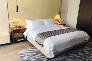 A hotel room with a bed, bedside tables, a nightstand, a chair, and a patterned rug. - Xinshenghao Hotel (Chengdu)