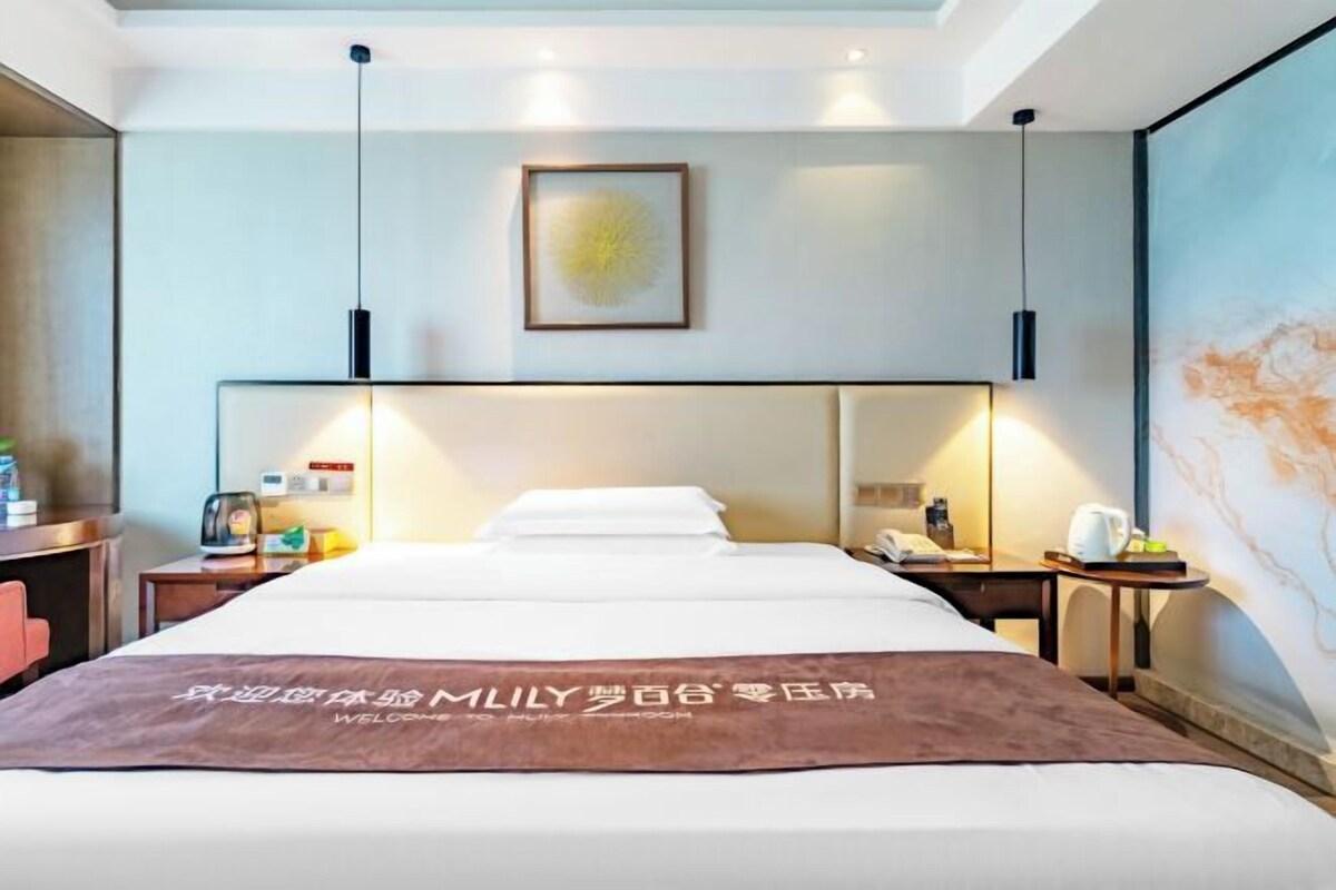 A hotel room with a large bed, bedside tables, a desk, a chair, and a wall-mounted artwork.