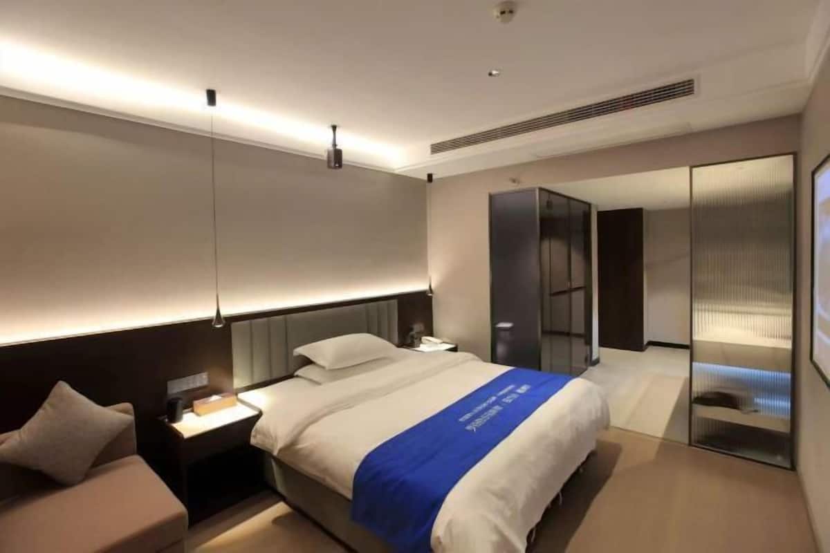 A modern hotel room with a large bed, bedside tables, a wardrobe, and a mirror.