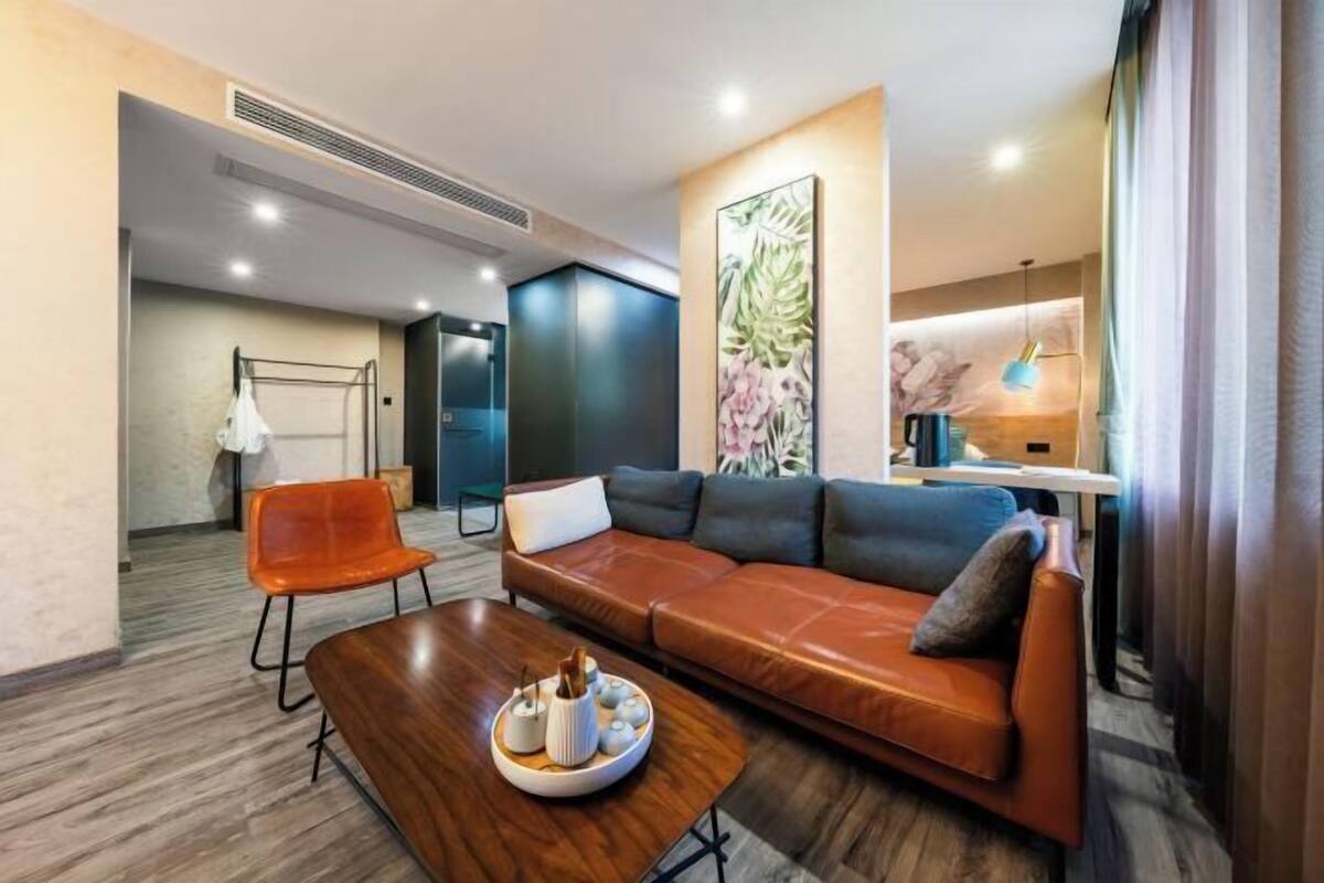 Una habitación de hotel moderna con un sofá de cuero, una mesa de centro de madera y una obra de arte floral grande en la pared.