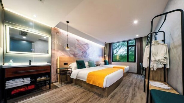 Una habitación de hotel moderna con una cama grande, mesita de noche, espejo y vistas a zonas verdes.