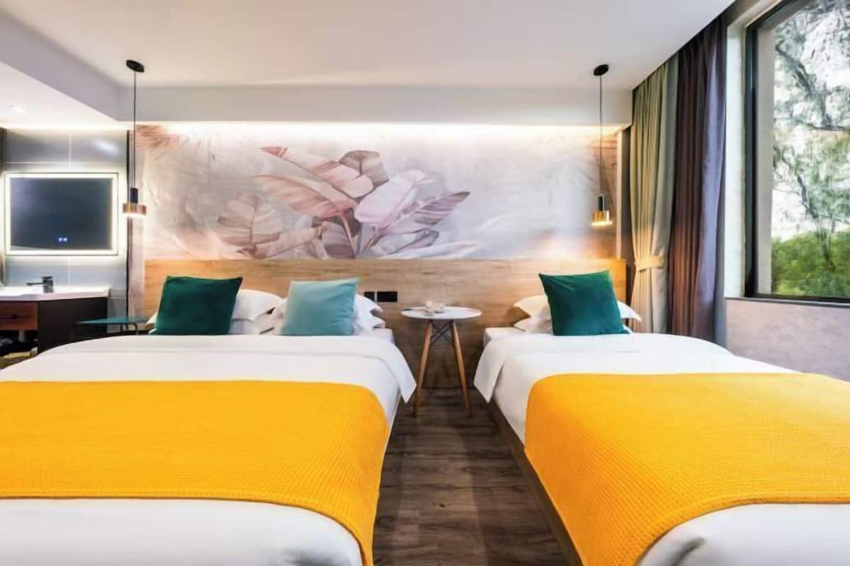 Habitación de hotel con dos camas, un ventanal grande, televisor instalado en la pared y una mesita redonda.