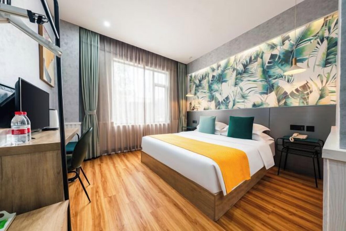 A hotel room with a bed, a desk, a chair, a TV, and a large window with curtains.