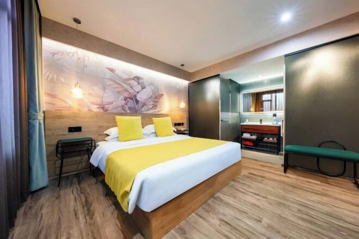 Habitación de hotel moderna con una cama grande, piso de madera, lámpara de pared e un banco.