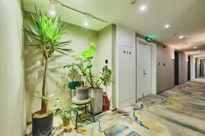 A hallway with potted plants, a fire extinguisher, and a door with a sign. - Leaf Time Art Hotel (Hangzhou)