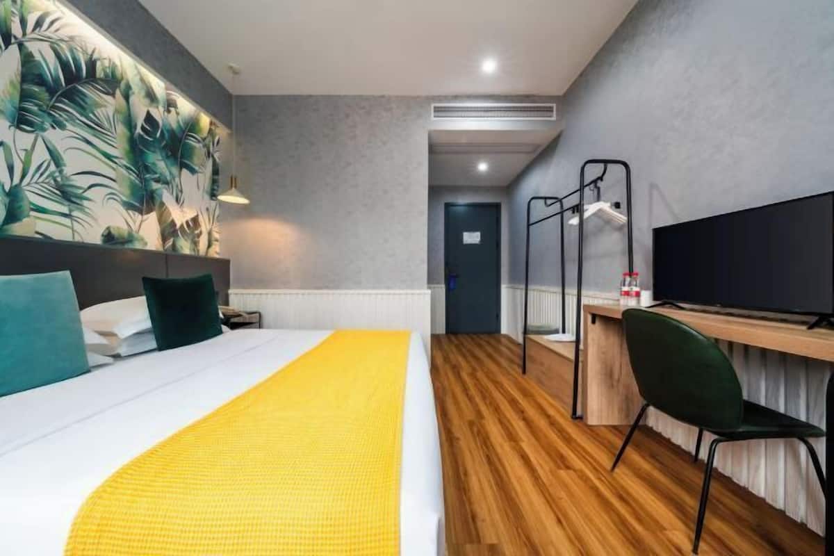 Habitación de hotel con cama, escritorio, silla, televisor y pared con estampado de hojas tropicales.