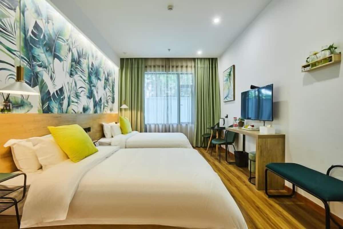 Habitación de hotel con dos camas, un escritorio, una silla, un televisor y un cuadro abstracto grande en la pared.
