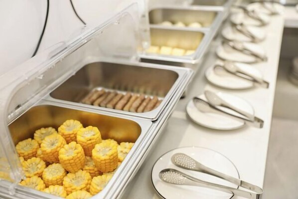 Un buffet proposant une variété de plats, notamment du maïs et d’autres spécialités.