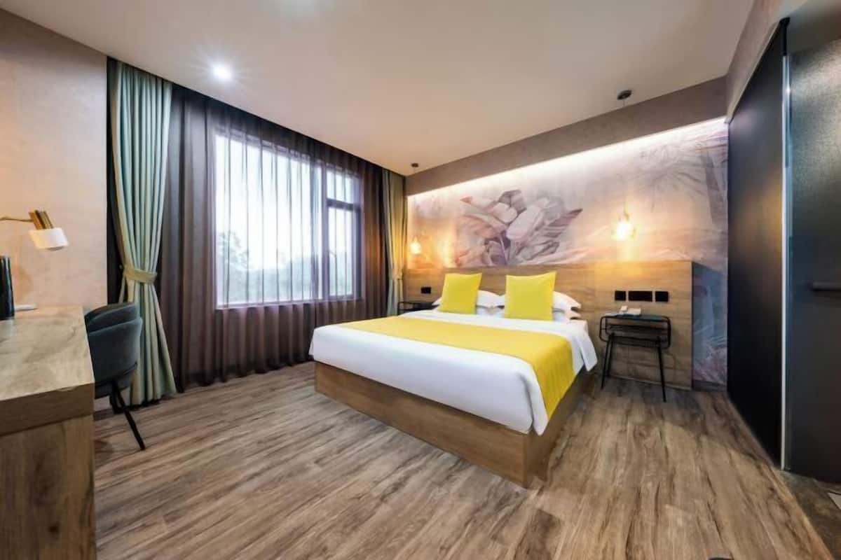 Habitación de hotel con una cama grande, un escritorio y una silla. Hay una ventana con cortinas, una lámpara de pared y un adorno en la pared.