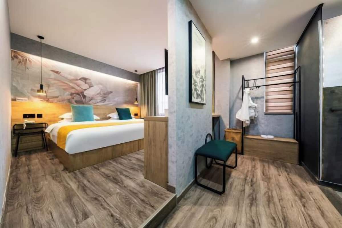 Una habitación de hotel moderna con cama, escritorio, silla, toallero y zona de ducha.