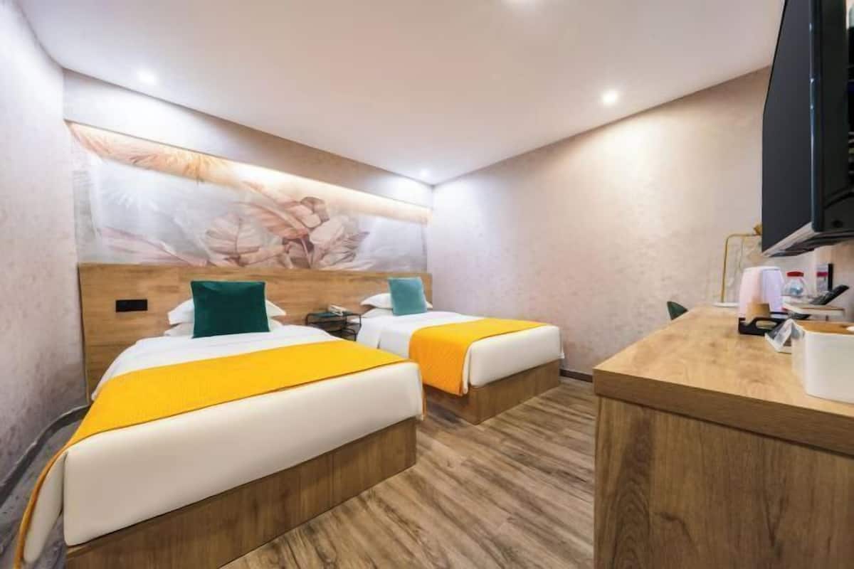Habitación de hotel con dos camas, un escritorio de madera, un televisor y una obra de arte colgada en la pared.
